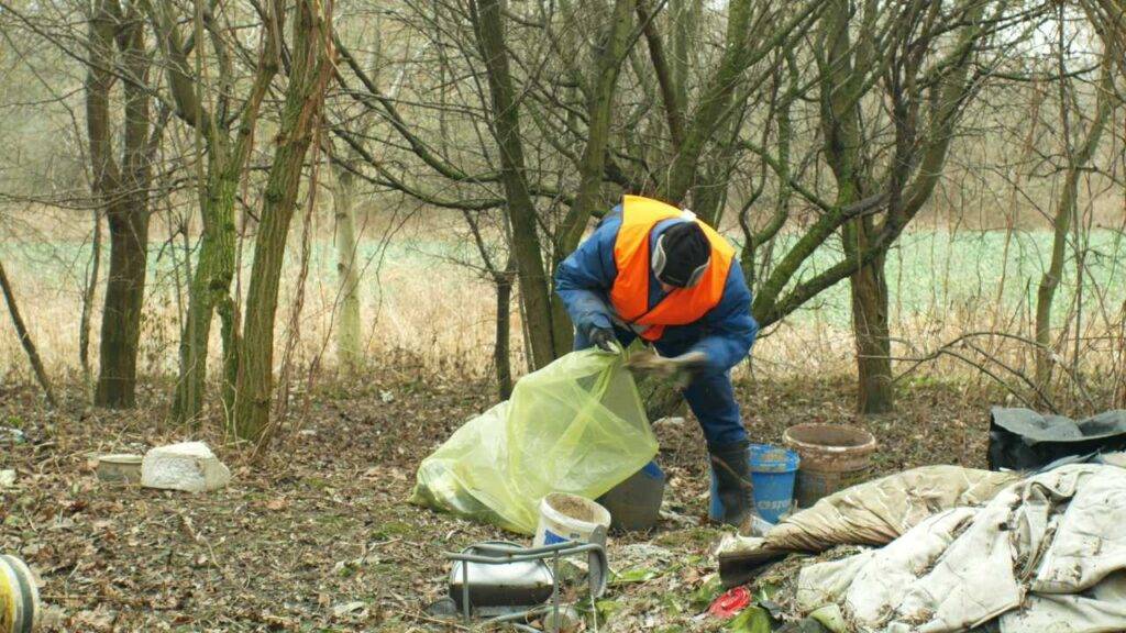 OLOMOUC, CZECH REPUBLIC, JANUARY 2, 2019: Man collect garbage rubbish gathers bag, forest landscape in endangered nature, black dump of human dirt of plastic trash various kinds
